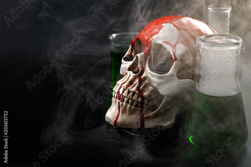 Biological warfare, chemical attack and genocide concept with a skull surrounded by chemistry flasks with smoke or mustard gas coming out of the green liquid with copy space