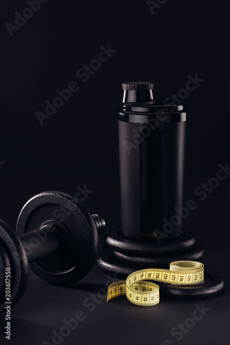 protein shaker with dumbbell and measuring tape isolated on black