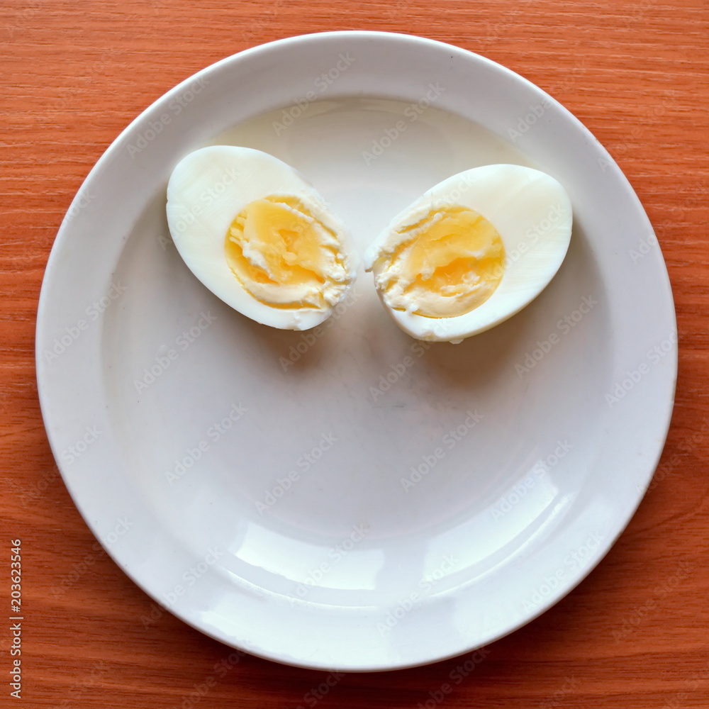 two halves hard boiled chicken egg on a white saucer and wooden table two halves hard boiled chicken egg on a white saucer and wooden table