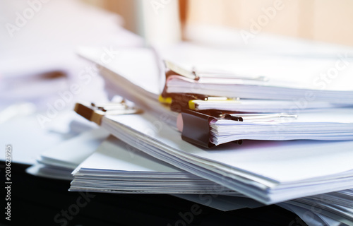 Stack of papers documents in archives files with clip papers on table at offices,  Busy offices and Pile of data unfinished folders on office desk indoor near window,  Business concept. photo