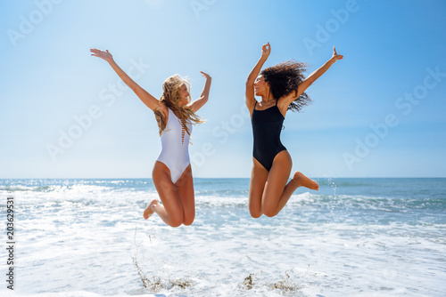 Two funny girls in swimsuit jumping on a tropical beach