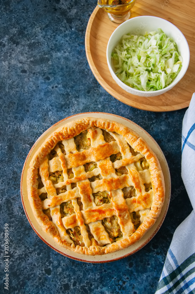 Homemade young cabbage pie from flaky dough served on a plate. blue stone background. Top view. Homemade young cabbage pie from flaky dough served on a plate. blue stone background. Top view.