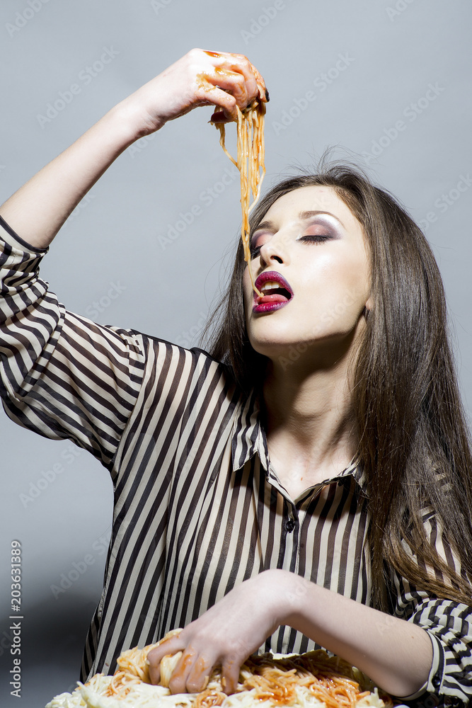 Fotka „Hungry girl have italian food meal. Sexy woman eat spaghetti with  hands. Woman eat pasta dish with tomato ketchup. Beauty model with makeup  and long brunette hair have dinner. Food, diet