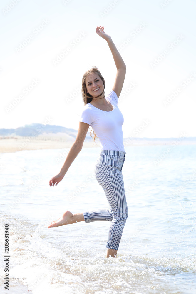 Hübsche blonde Frau hüpft durch seichtes Wasser am Meer Hübsche blonde Frau hüpft durch seichtes Wasser am Meer