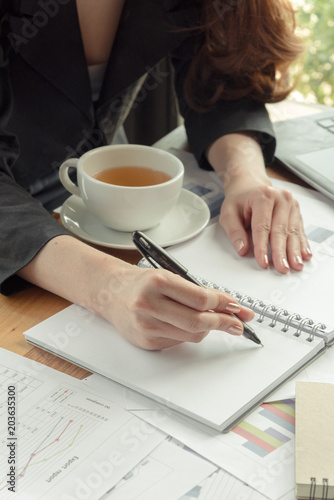 business woman writing in book with a cup of coffee in office
