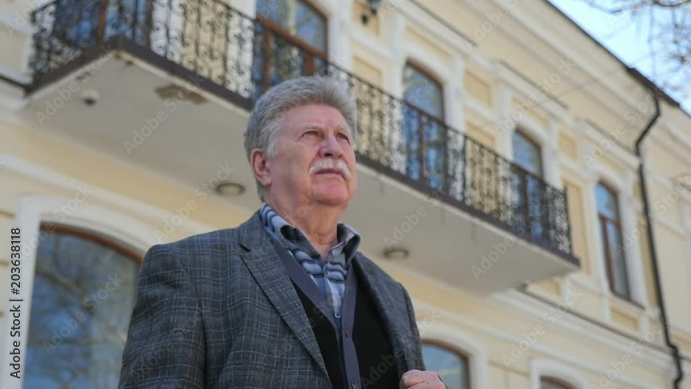 A 180 degeree view of a confident senior man with mustache smiling and standing at a historic building on a sunny day in slow motion A 180 degeree view of a confident senior man with mustache smiling and standing at a historic building on a sunny day in slow motion