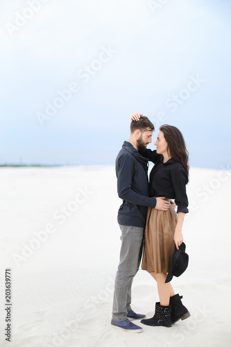 Caucasian female person hugging man in winter snow background, wearing skirt, black blouse and keeping hat. Concept of fashionable look and romantic love photo session. photo