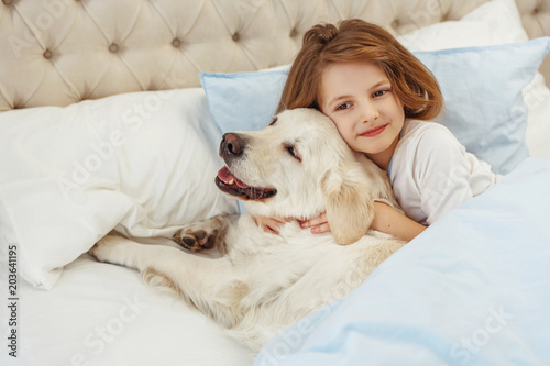 Beautiful little girl with golden retriever dog in a bed