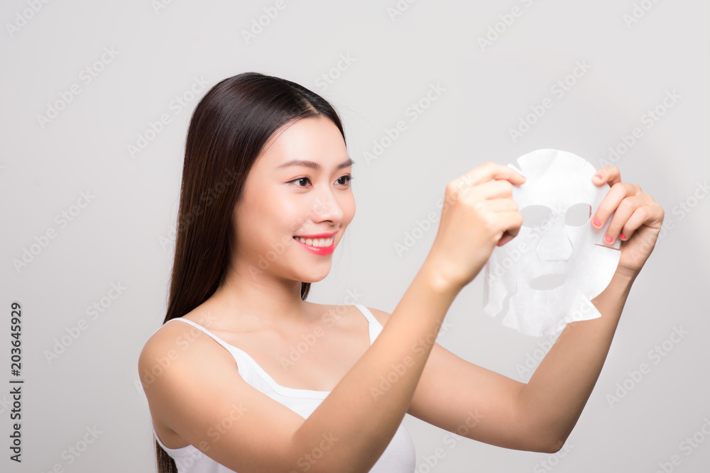 Beautiful asian woman applying paper sheet mask on her face white background. Beautiful asian woman applying paper sheet mask on her face white background.