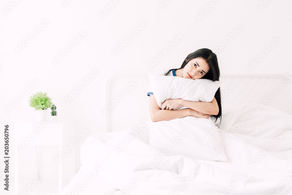 Beautiful woman smiling to camera and relaxing with pillow on the bed in her room at home Beautiful woman smiling to camera and relaxing with pillow on the bed in her room at home