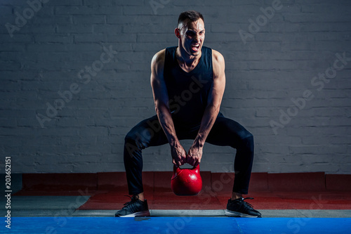 Young man strengthens the muscles of the hands of red weights in the gym on a black background