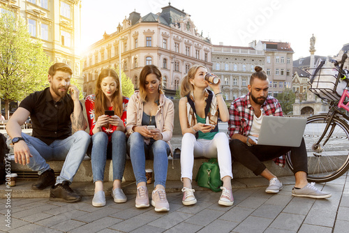 Glückliche Studenten genießen ihren sorglosen Lebensstil in der Stadt sitzen auf der Straße mit Gadgets an einem sonnigen Nachmittag