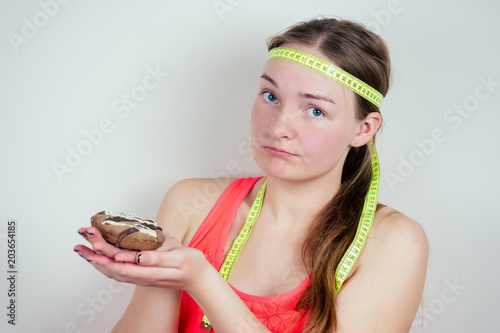 Portrait of a young and beautiful teenage girl holding a biscuit and measuring tape around her head. concept of anorexia