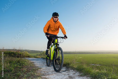 A cyclist in an orange hoodie rides a bike along a mountain path. The concept of extreme sports. Training in the mountains.