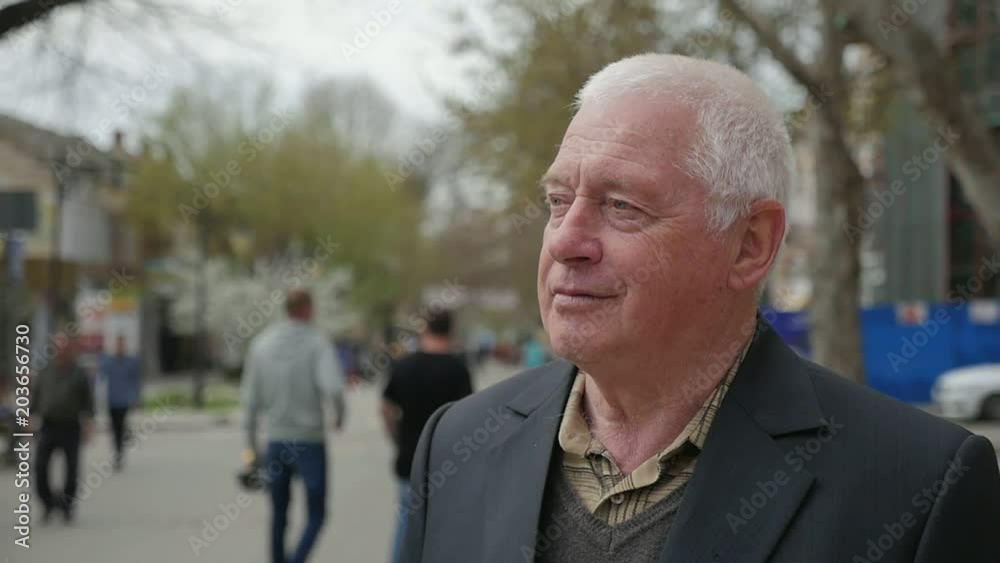 A profile of a confident white-headed man smiling and sitting on a bench in a street with trees and modern houses in spring in slo-mo A profile of a confident white-headed man smiling and sitting on a bench in a street with trees and modern houses in spring in slo-mo