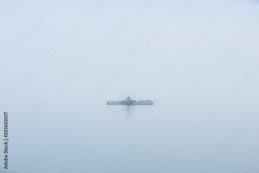 Fine art minimalist image of derelict pier remains at sea during foggy morning giving appearance of ruins floating
