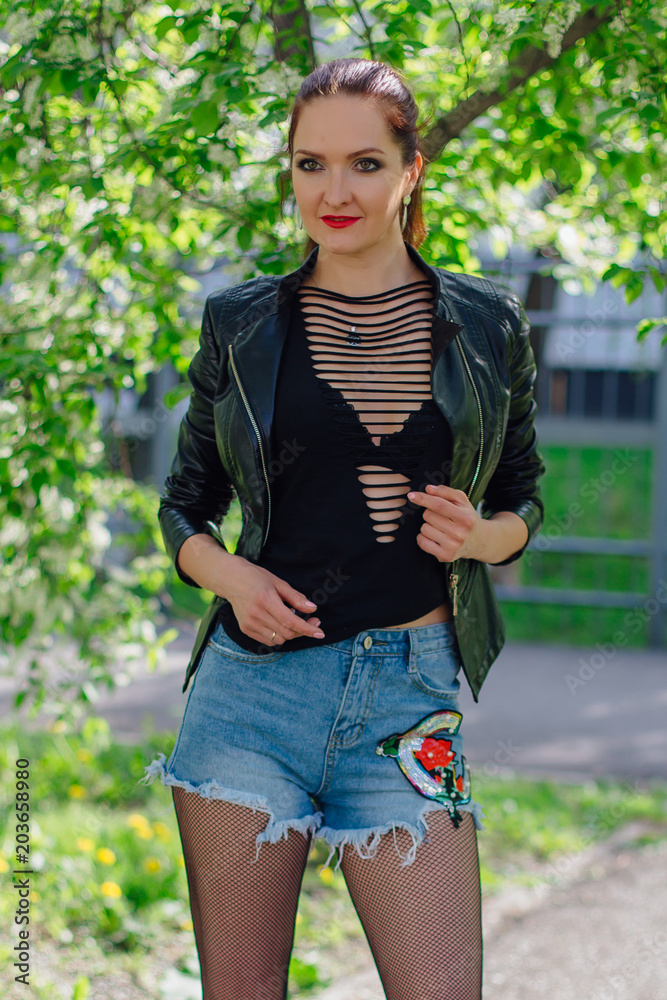 Charming woman dressed in a leather jacket near bird-cherry tree Charming woman dressed in a leather jacket near bird-cherry tree