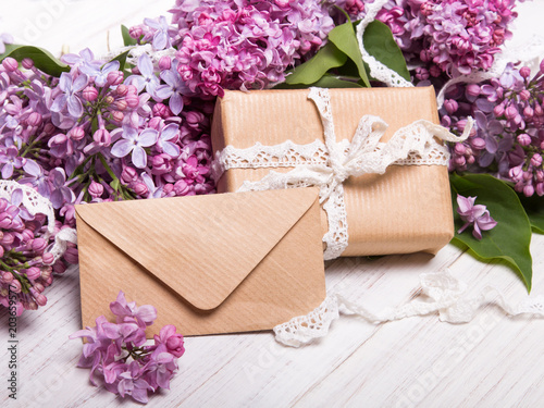 Prezent z kokardą i liścik z życzeniami otoczony kwiatami bzu, Świąteczna kompozycja z okazji Dnia Matki lub urodzin