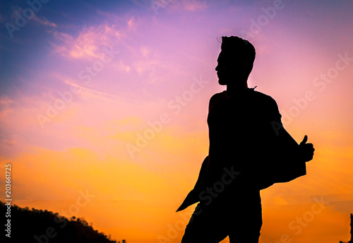 The silhouette of a man  his arms muscles show strong on the background of the sunset. By Phawat