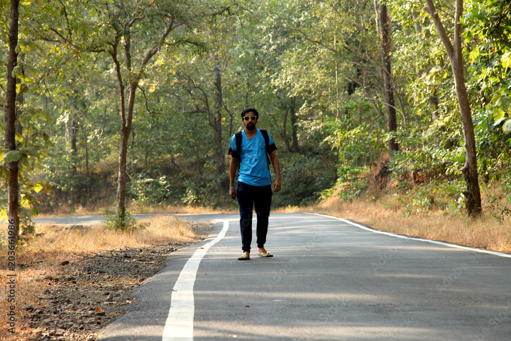 Travel concept man carrying backpack walking on the road passes through beautiful forests.