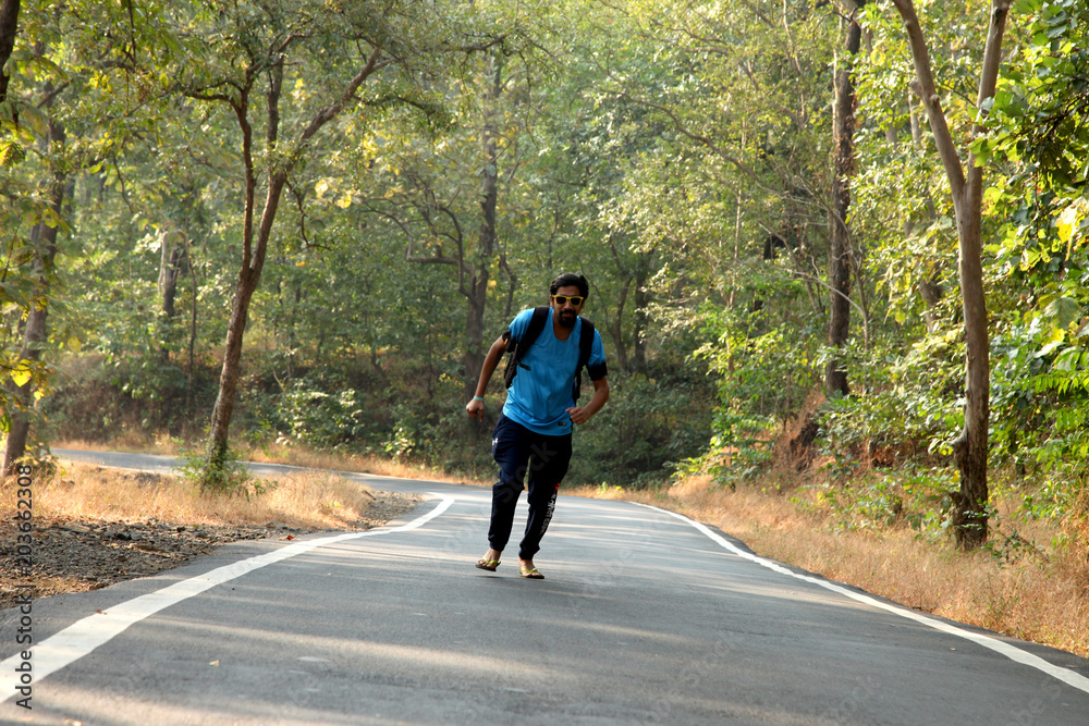 Travel concept man carrying backpack walking on the road passes through beautiful forests.