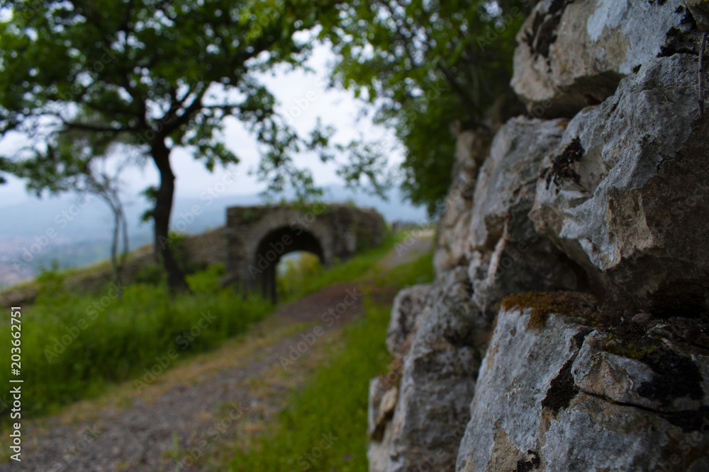 Sentiero di campagna lungo le mura di un castello, con ponte romano in lontananza - obrazy, fototapety, plakaty 