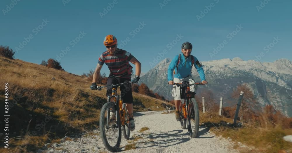 Close-up tracking shot of mountain bikers cross-country cycling with amazing mountains in background. Close-up tracking shot of mountain bikers cross-country cycling with amazing mountains in background.