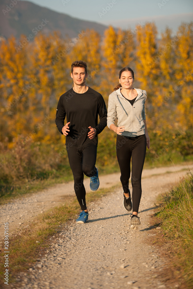 Obraz premium Young veautiful couple runs on a path in park on autumn afternoon