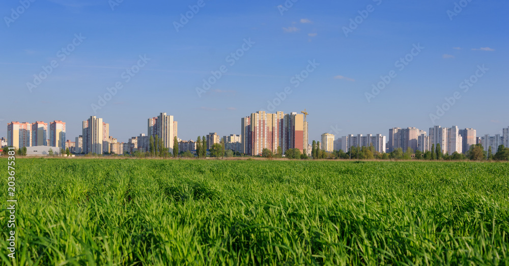 Green agricultural field with urban skyline. City and nature. Horizon with residential buildings in Kiev, Ukraine