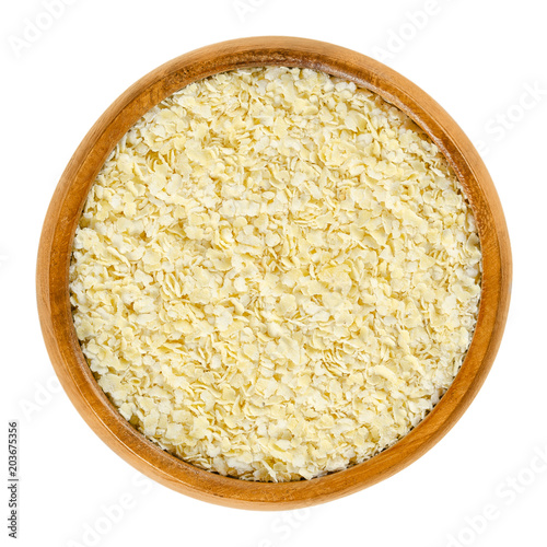 Millet flakes in wooden bowl. Light, yellow rolled millet, used for porridge, muesli and baking. Wheat and gluten free grain. Isolated macro food photo close up from above on white background.