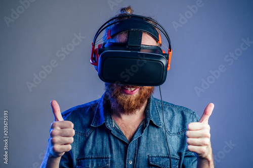 portrait of a young man in virtual reality points points his finger gray wall background. The concept of games in the mask of virtual reality