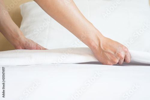 Male Hand set up white bed sheet in room hotel.