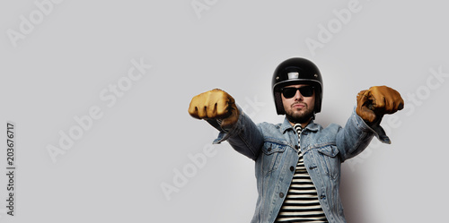Fotografia Young biker in a blue denim jacket pretending to ride a motorcycle isolated on white background