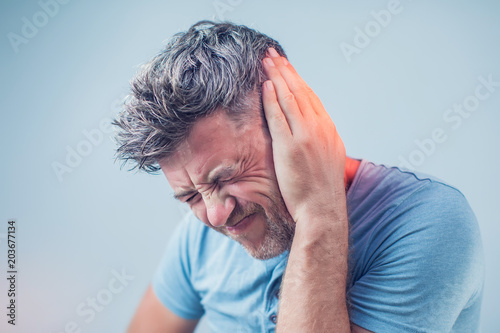 male having ear pain touching his painful head isolated on gray background photo