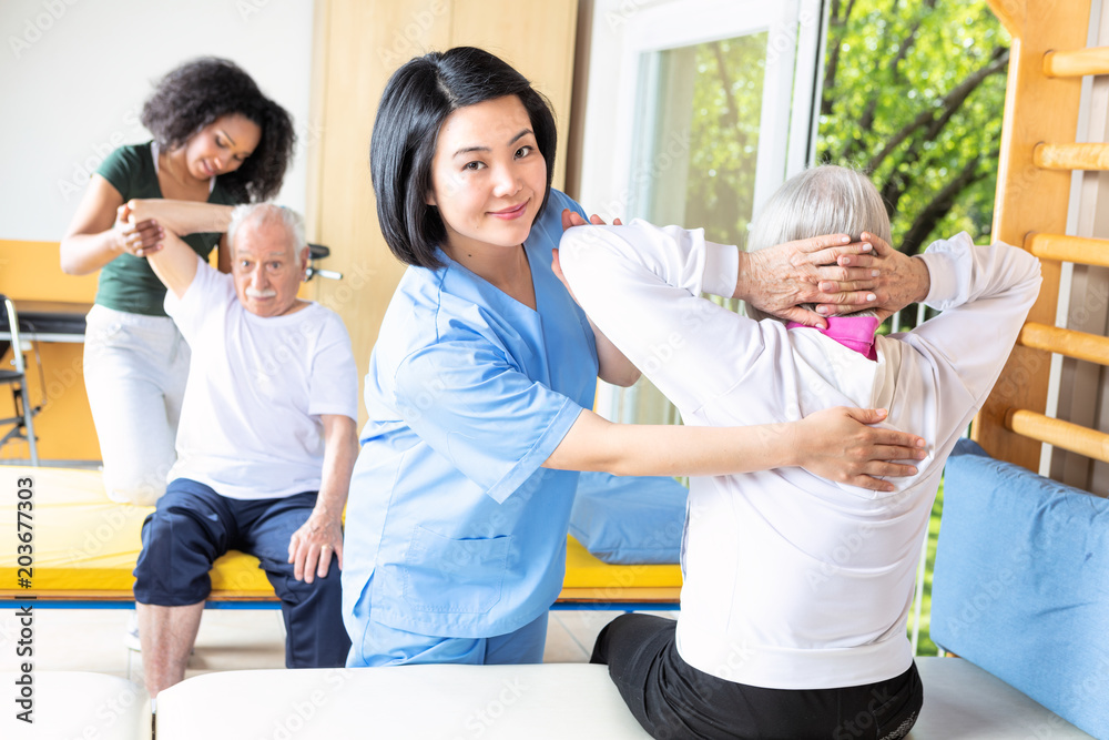 Asian and african nurses helping elder couple at rehab facility gym