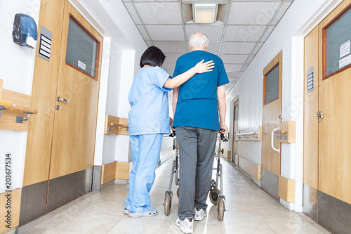 Fototapeta Asian nurse helping elder man walking in rehab facility