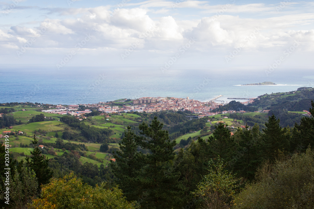 Scenic views of green landscape with Bermeo fishing town by the sea on the background, Basque Country