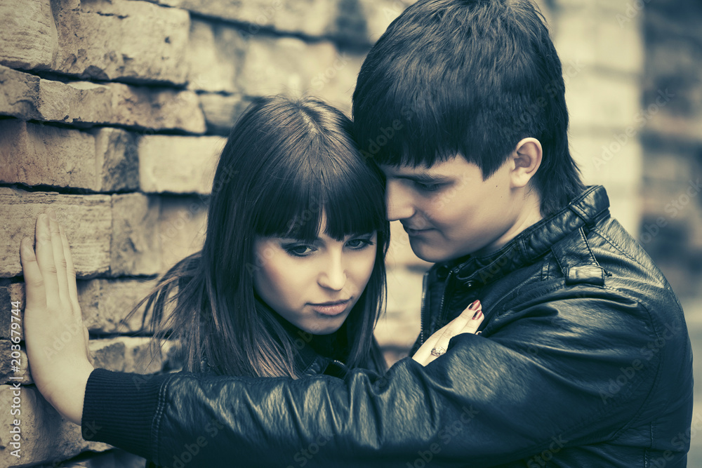 Happy young fashion couple in leather jackets at the brick wall