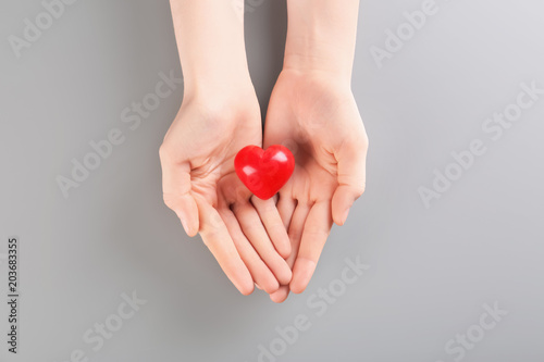 Fototapeta Naklejka Na Ścianę i Meble -  Woman holding small red heart on gray background. Heart attack concept