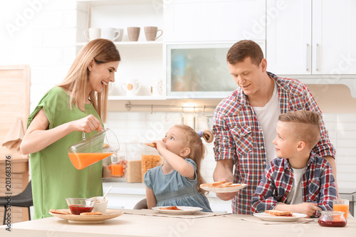 Parents and cute little children having breakfast with tasty toasted bread at table in kitchen