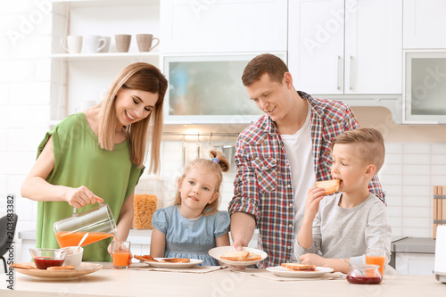 Parents and cute little children having breakfast with tasty toasted bread at table in kitchen