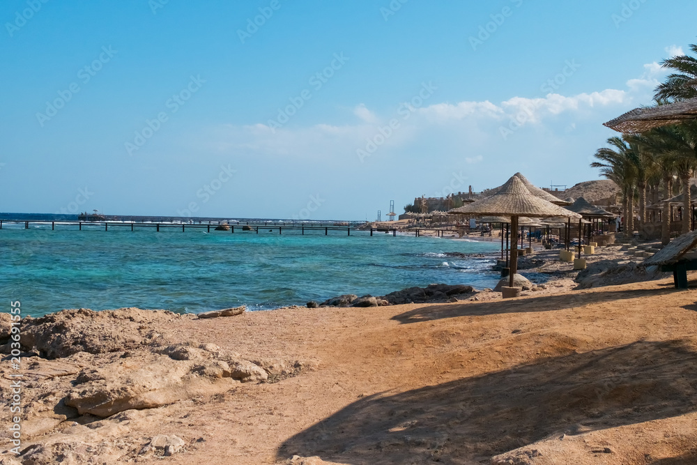 Resort in Egypte. View of beach with umbrellas, sand, blue sky and water.