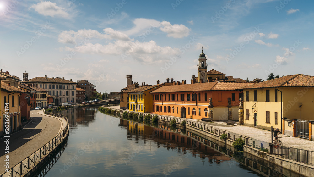 Cityscape of Gaggiano, just outside of Milan. Colourful houses reflected in the Naviglio Grande canal waterway and purposely blurred cyclist.