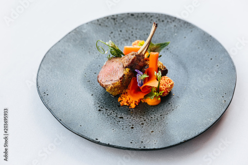 Modern French cuisine: Close up roasted Lamb neck & rack served with carrot, yellow curry served in black stone plate.