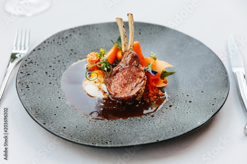 Modern French cuisine: Roasted Lamb neck & rack served with carrot, yellow curry pouring lamb sauce. Served in black stone plate