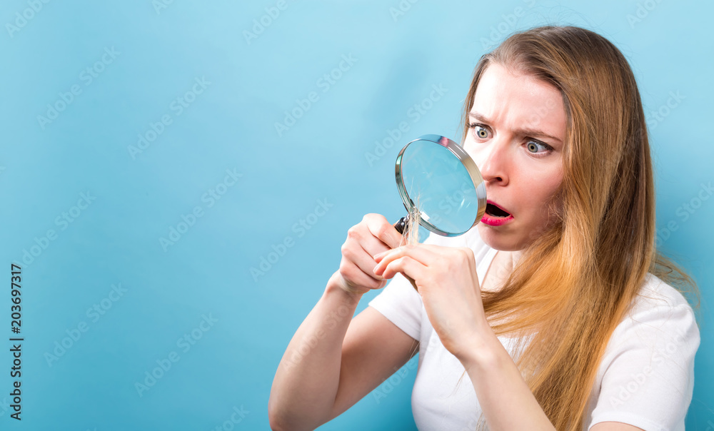 Beautiful woman inspecting her hair with a magnifying glass on a solid background Beautiful woman inspecting her hair with a magnifying glass on a solid background