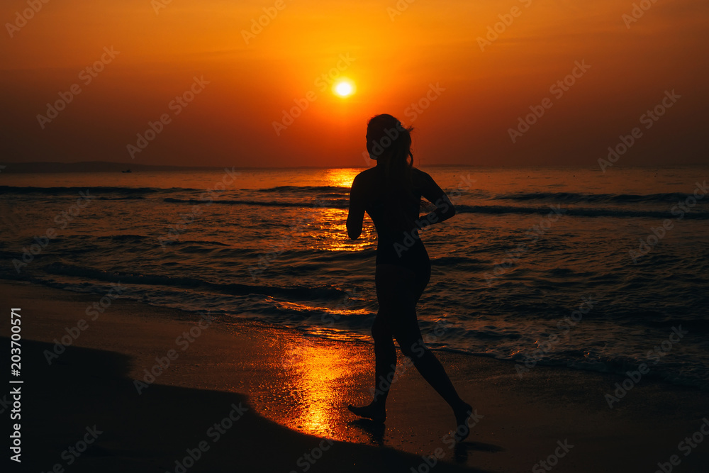 silhouette of a girl running by the sea on the beach at sunrise