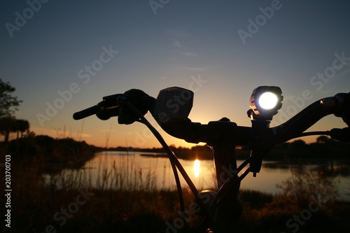A bicycle is parked with its white night light illuminated at sunset near a lake at Quiet Waters Park, Deerfield Beach, Florida