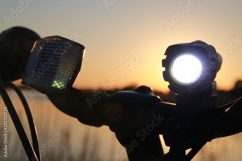 A bicycle is parked with its white night light illuminated at sunset near a lake at Quiet Waters Park, Deerfield Beach, Florida