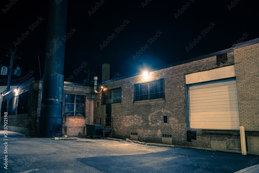 Dark and eerie urban city alley with vintage warehouses and factory buildings at night
